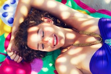 A woman in a blue bathing suit lying on a colorful beach towel while the sun pokes through