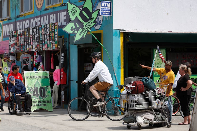 A man riding a bike down a street with a marijuana shop