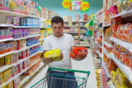 A man at the supermarket deciding between a generic item and one with a famous brand name