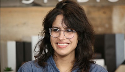 Desiree Akhavan in a pale navy linen shirt and translucent glasses, smiling