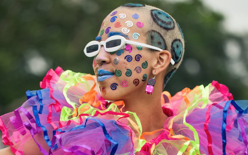 A girl posing in a grey tank and skirt, a tulle multicolored collar, blue smiley faces painted in he...
