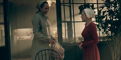 Two woman dressed as maids in white and red clothes acting in a scene from the series Handmaid's Tal...