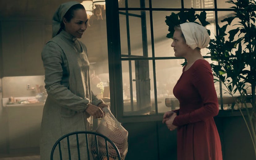 Two woman dressed as maids in white and red clothes acting in a scene from the series Handmaid's Tal...