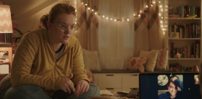 Barb from Stranger Things sitting on a bed and looking at a computer