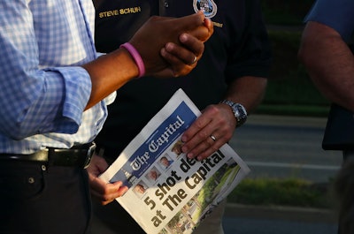 A policeman holding a newspaper with a headline about dead people at The Capital