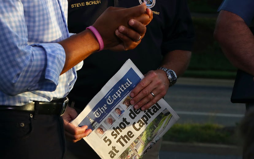 A policeman holding a newspaper with a headline about dead people at The Capital