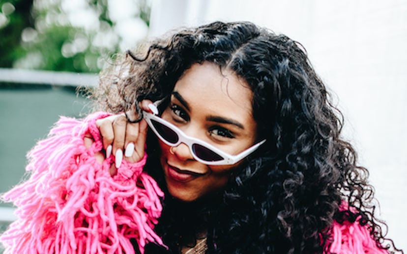 Anaya Ivy in cat eye sunglasses, a pink fringe jacket, black romper accessorized with a white fanny ...