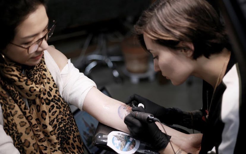 Woman tattoo artist tattooing another woman.