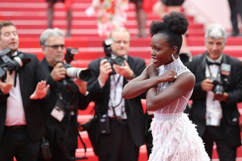Lupita Nyong'o in a white dress crossing her arms on the Cannes Film Festival red carpet