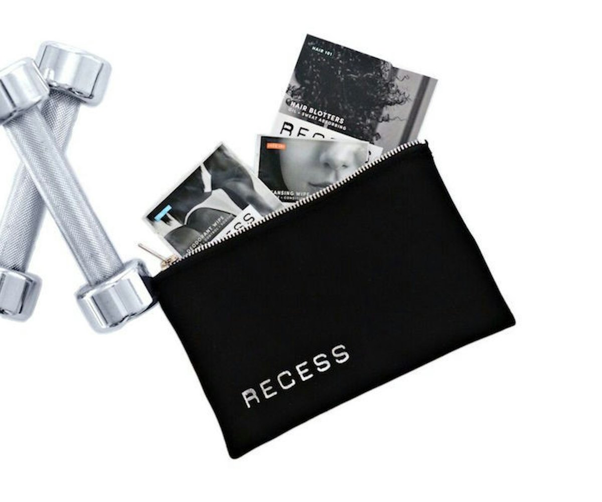 Two workout weights next to a Recess beauty line products and a Recess toiletry bag.