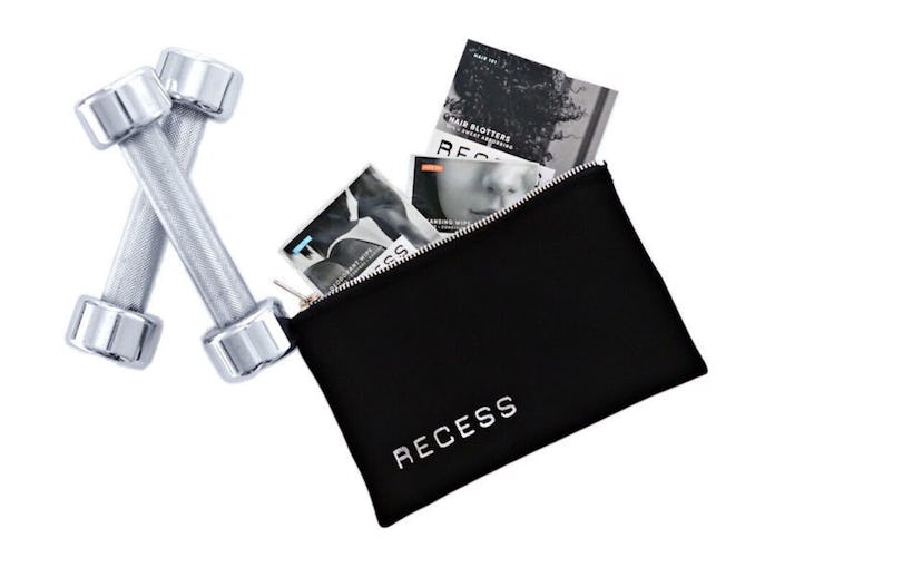 Two workout weights next to Recess beauty line products and a Recess toiletry bag
