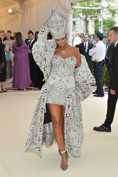 Rihanna at the Met gala in a bejeweled pope hat and robe walking the red carpet