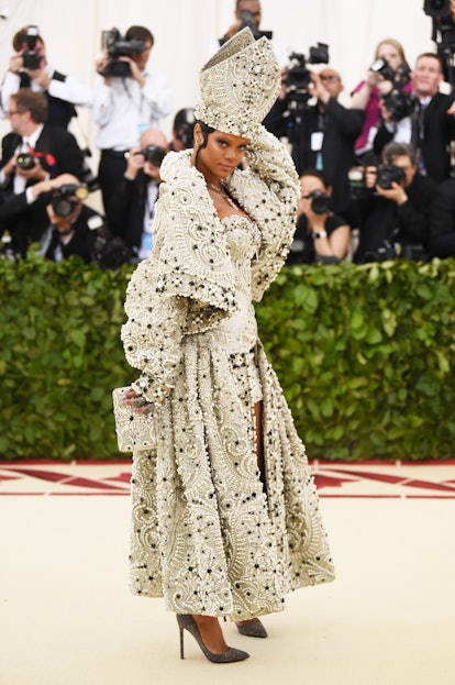 Rihanna at the Met gala in a bejeweled pope hat and robe posing in front of photographers   