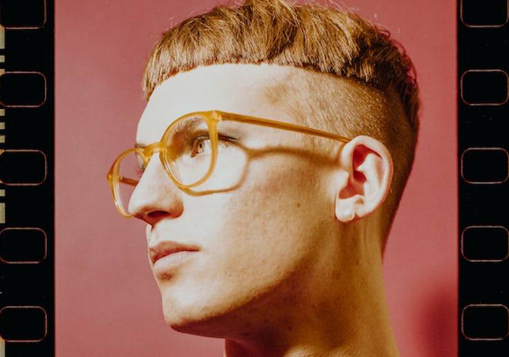 Gus Dapperton with a bowl cut hairstyle and orange glasses