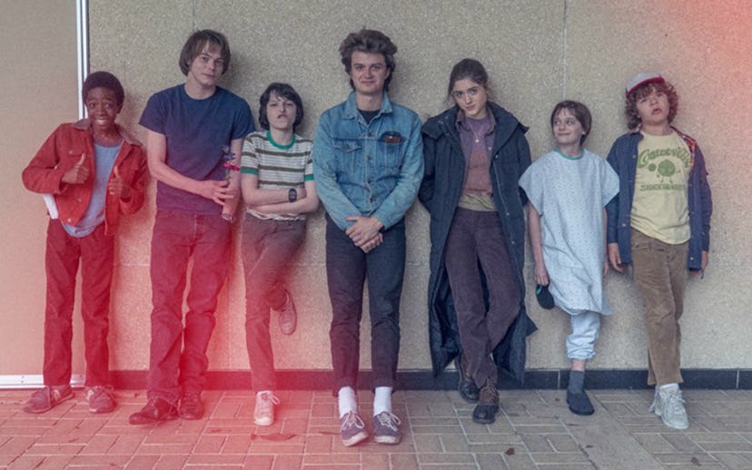 The cast of Stranger Things, two teenagers and two children, a boy and a girl, leaning against the w...