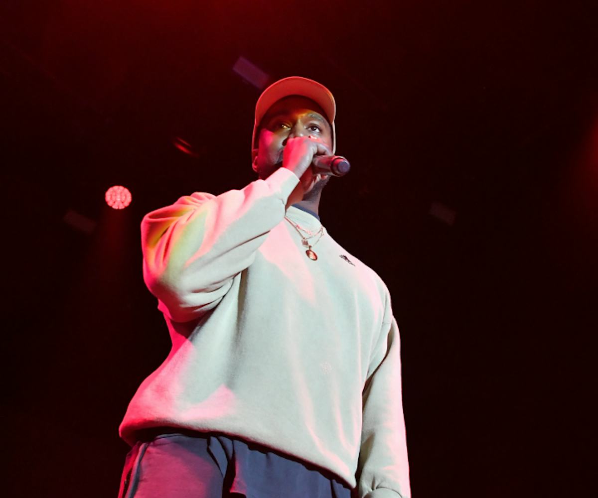 Kanye West on stage in a white sweatshirt and a white cap with a microphone in his hands 