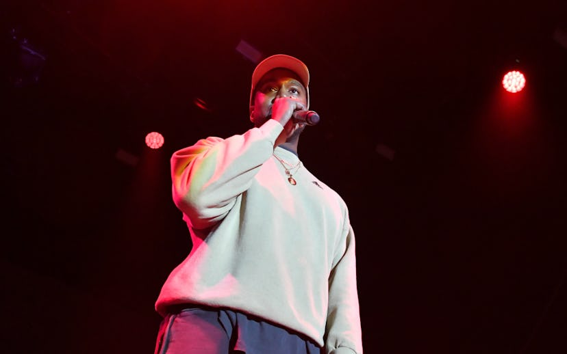 Kanye West on stage in a white sweatshirt and a white cap with a microphone in his hands 