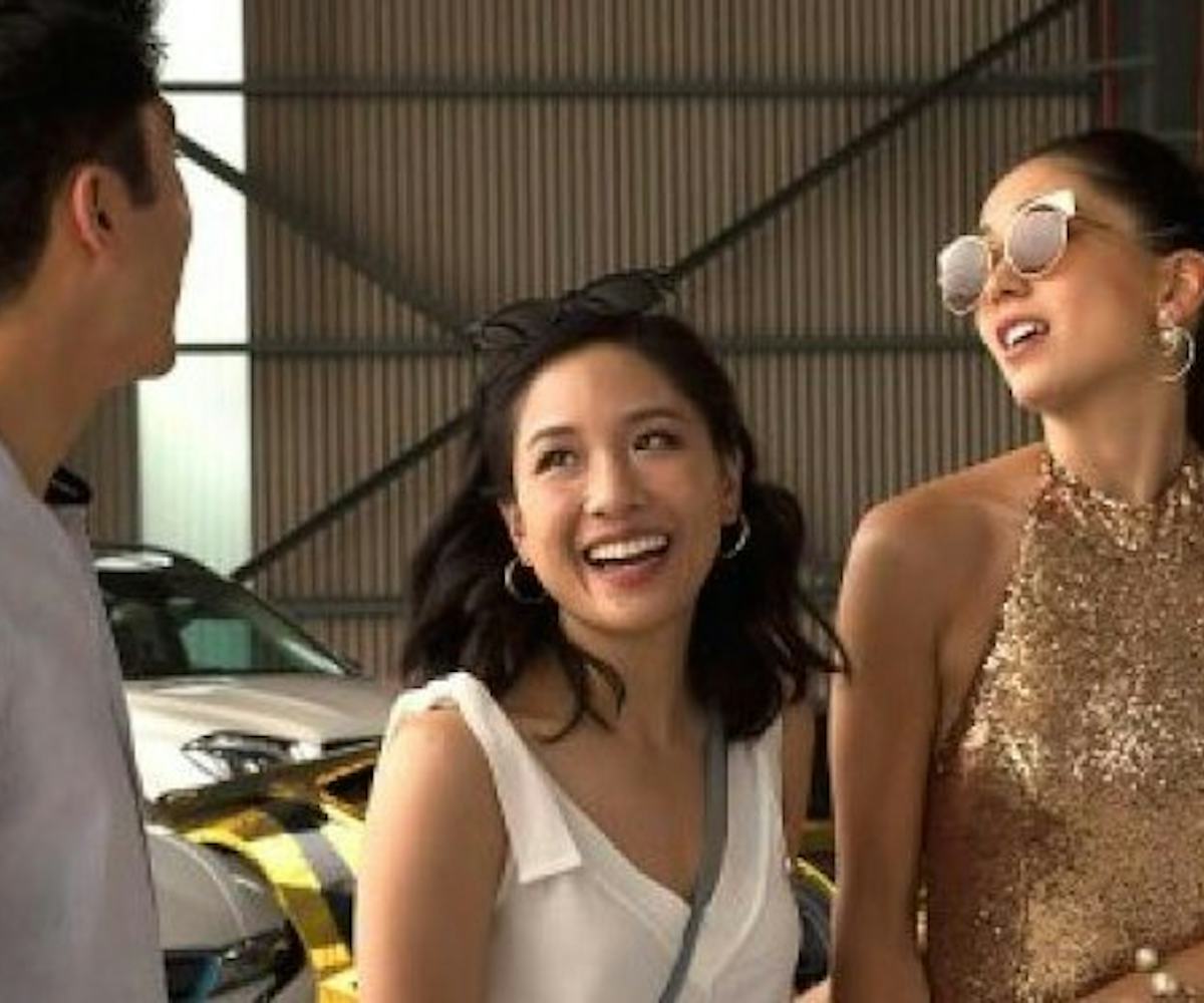 A shot of Henry Golding, Constance Wu, and Jin Lusi in the movie Crazy Rich Asians talking and smili...