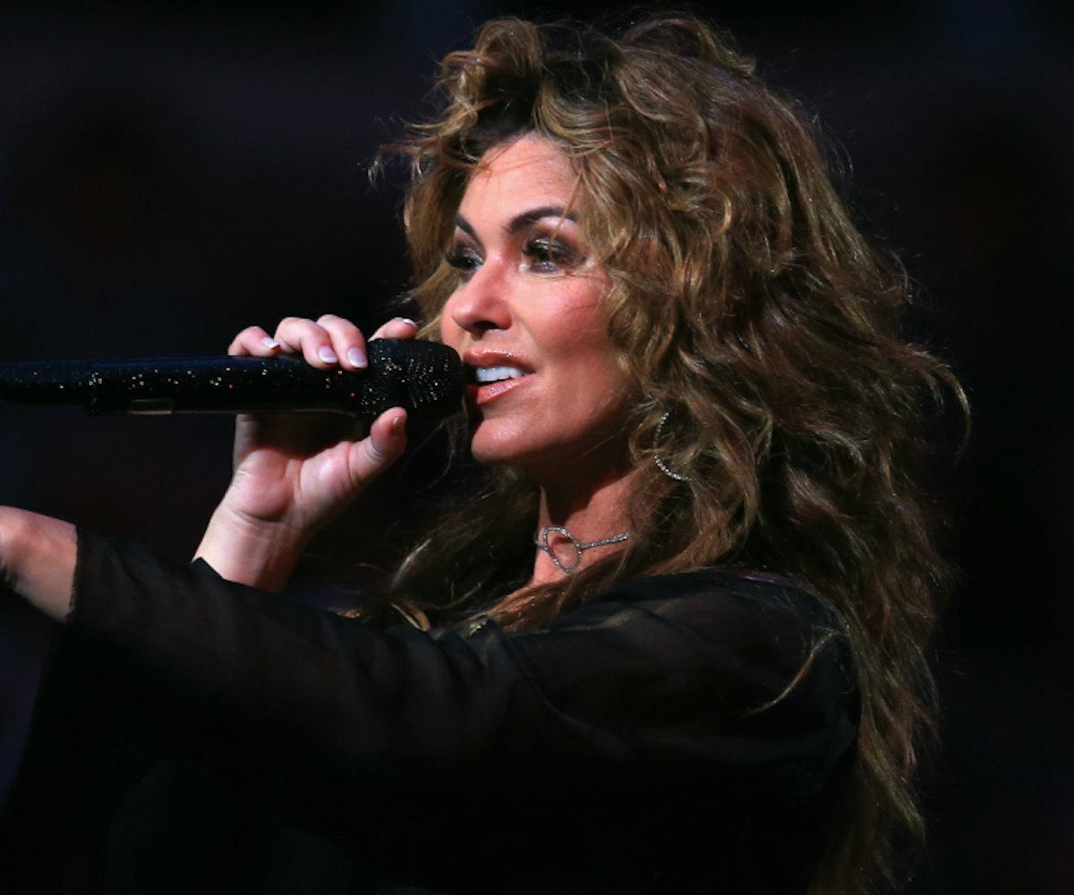Shania Twain holds a glittery black microphone on stage and points toward the audience