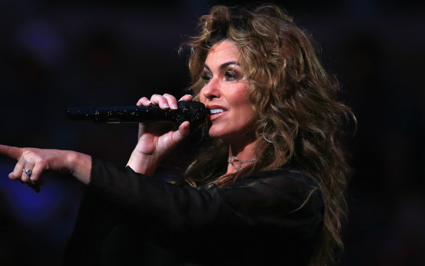 Shania Twain holding a shimmery black microphone on stage and pointing toward the audience