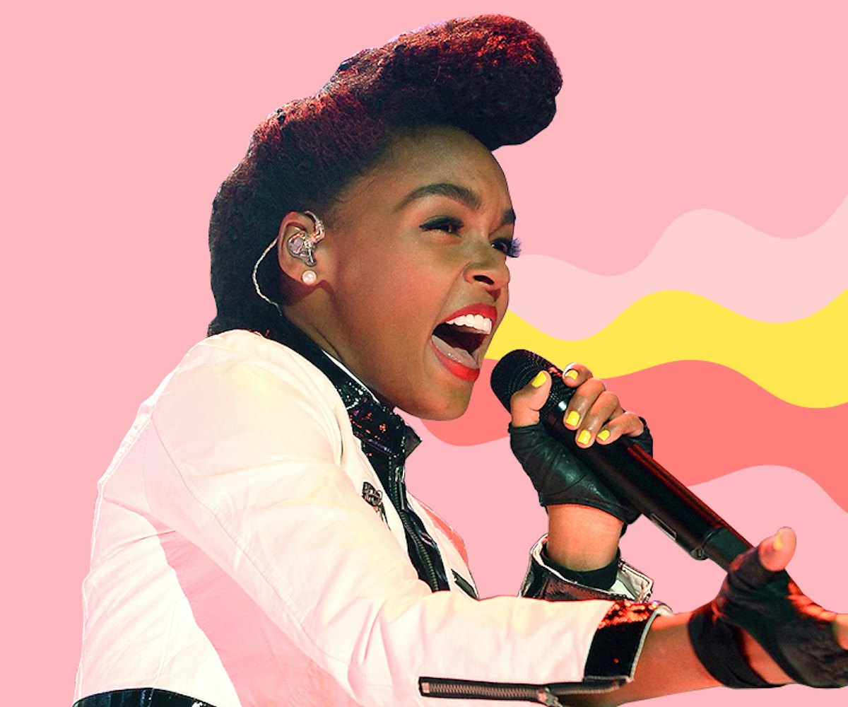 Janelle Monáe singing in front of the pink background while wearing a white jacket