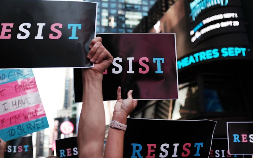 Protesters holding black paper with blue, red-and-white text saying "Resist" against Trump's new pol...