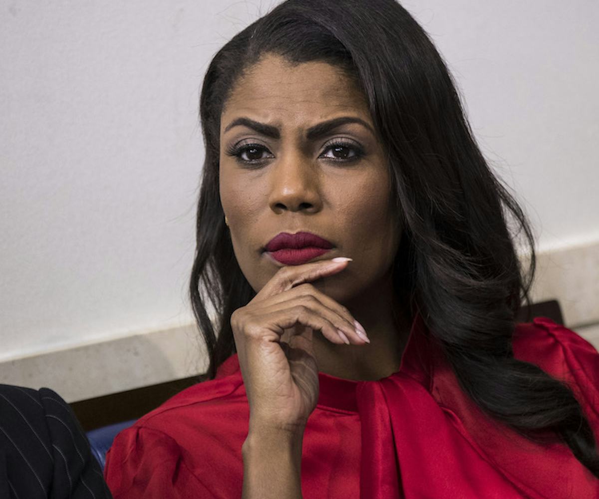 Omarosa Manigault sitting in a red blouse and a thoughtful look with a hand leaned on her chin