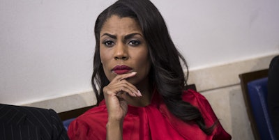 Omarosa Manigault sitting in a red blouse and a thoughtful look with a hand leaned on her chin