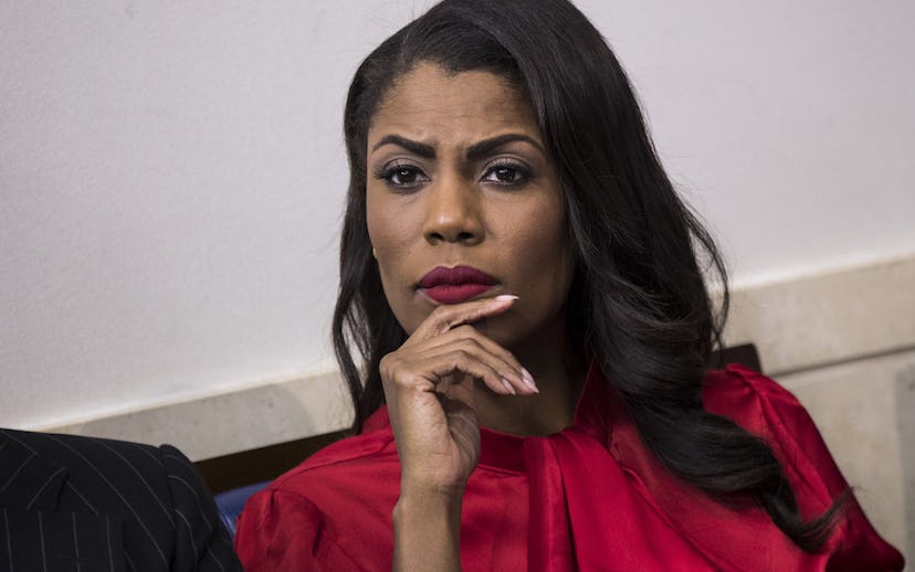 Omarosa Manigault sitting in a red blouse and a thoughtful look with a hand leaned on her chin