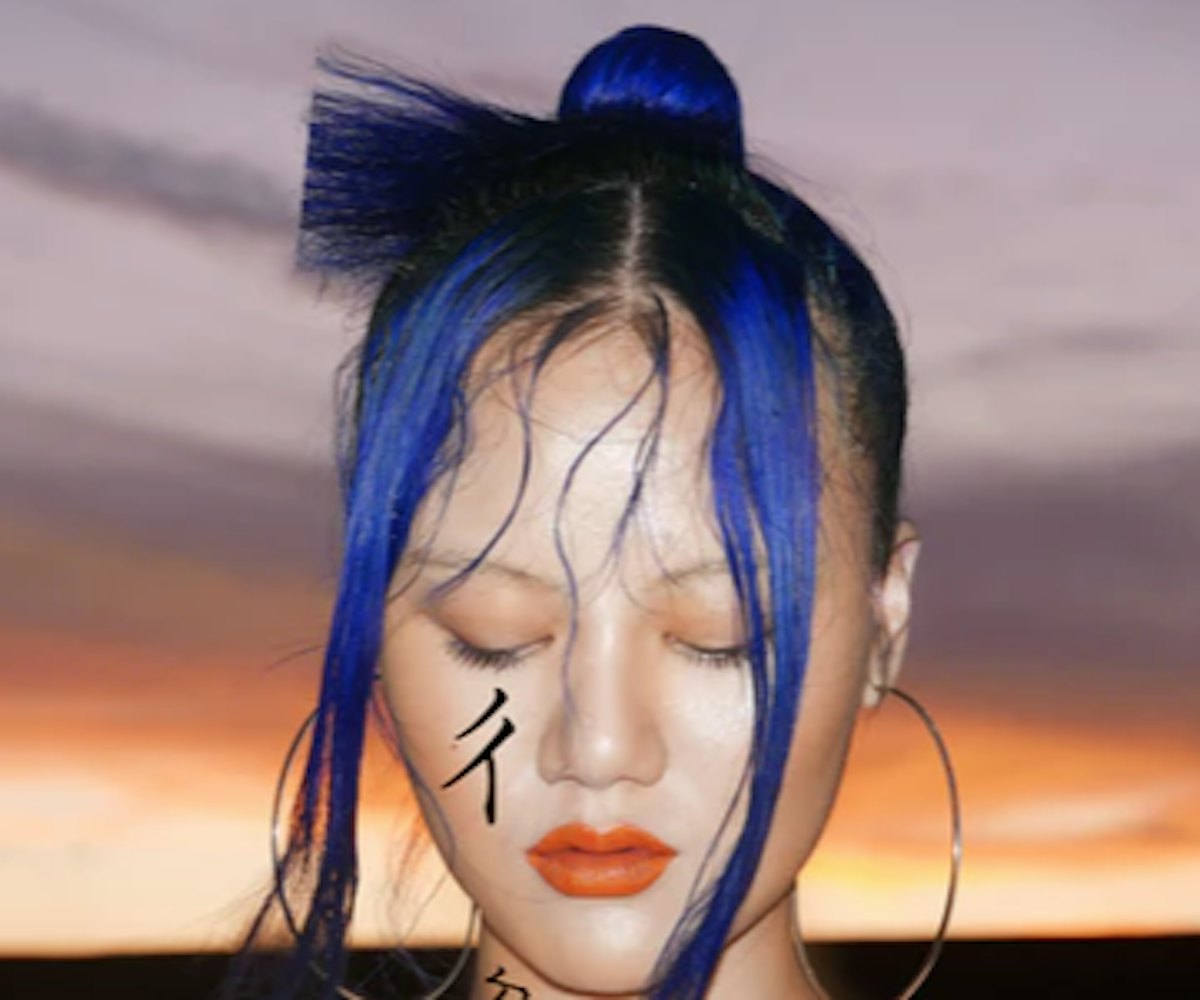John Yuyi with blue-and-black hair and a tattoo on her cheek with the dusk sky behind 