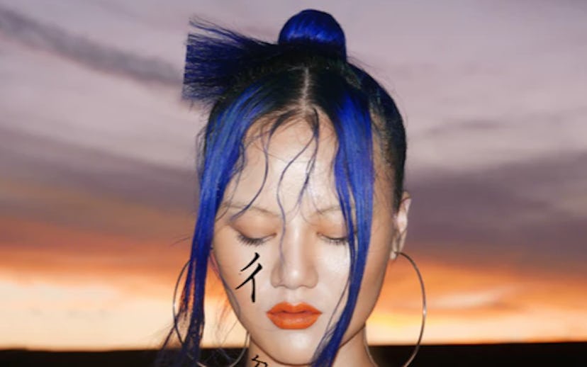 John Yuyi with blue-and-black hair and a tattoo on her cheek with the dusk sky behind