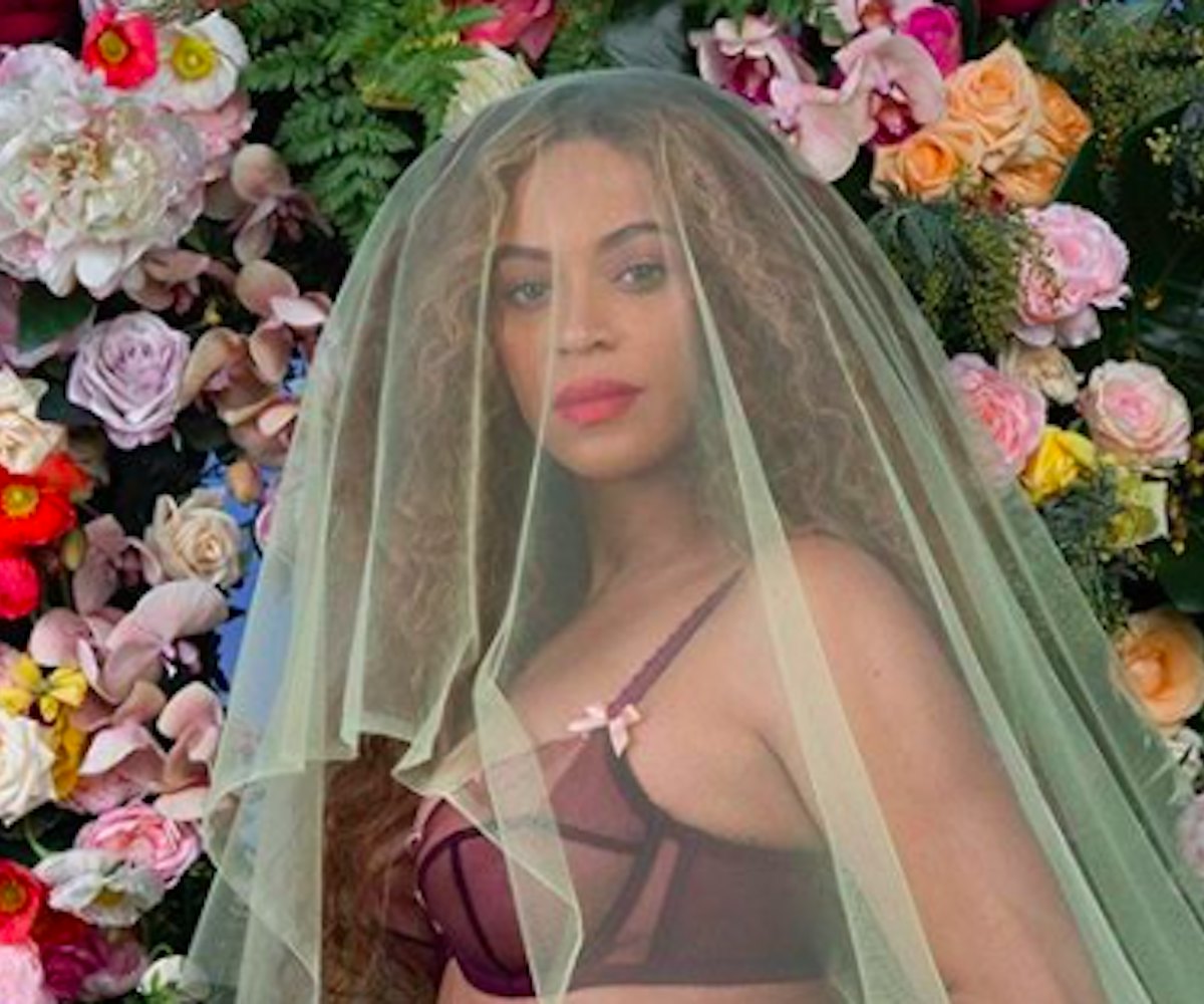Beyonce kneeling and holding her pregnant stomach in blue denim shorts with a yellow tulle veil and ...