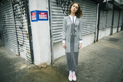 A brunette woman in a black-white-grey long-sleeved dress with the imitation print of a suit and pin...