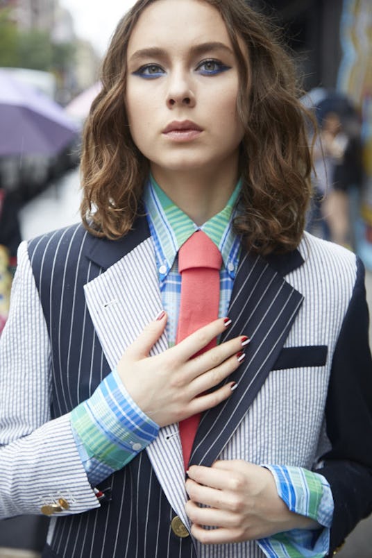 A brunette girl in a blue-green checked shirt and black and white patchwork blazer with orange tie b...