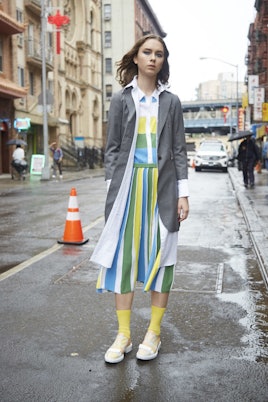 A girl in a pastel green-yellow-white dress, white shirt and grey coat by Thom Browne
