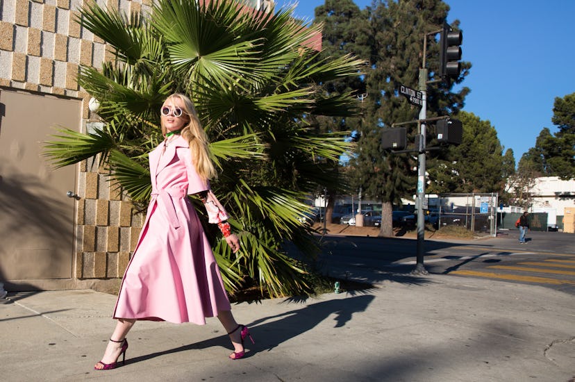 Kathryn Newton in a pink trench coat and glasses walking down the street