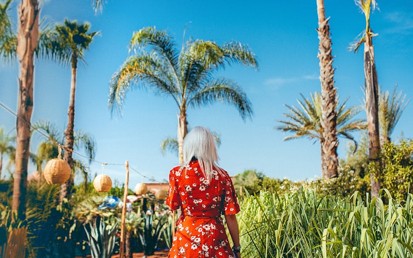 A blonde girl in a vibrant flowery outfit walking under palm trees on a sunny day