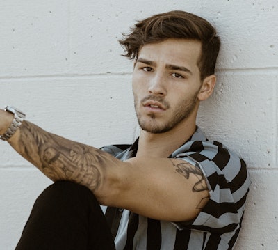 Singer and songwriter Jacob Whitesides sitting down wearing a black and gray striped shirt on his ne...