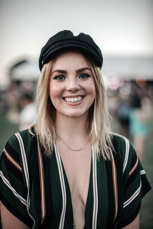 Gorgeous blonde girl posing with a big smile while wearing a black hat, dark colored outfit, and a s...