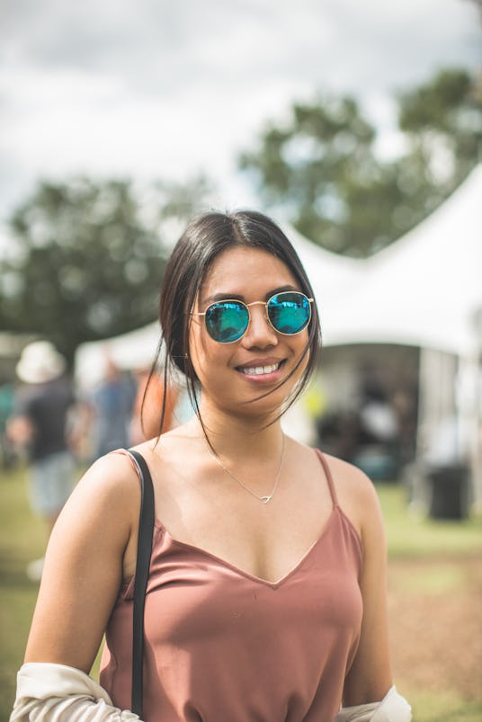 Girl posing with a smile, while wearing blue colored sunglasses and a brown t-shirt