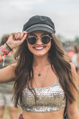 Girl posing in a silver crop top paired with a black hat, round black sunglasses, and a bold burgund...