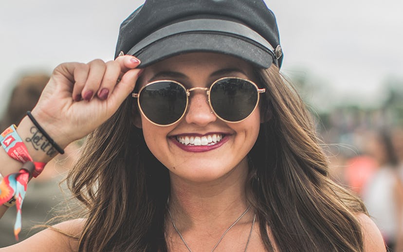 Girl posing with a black hat, round black sunglasses, and with a bold burgundy lipstick