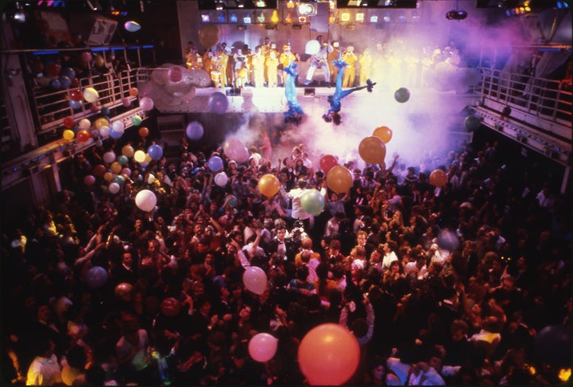 A full nightclub of people enjoying music with balloons and steam effects