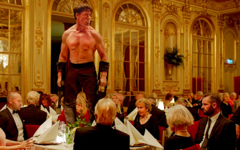 Actor Terry Notary standing on a table while not wearing a shirt with people surrounding him and din...