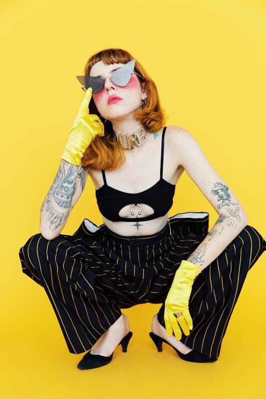 Alanna Pearl wearing sunglasses and a black top with black and yellow pants and yellow gloves 