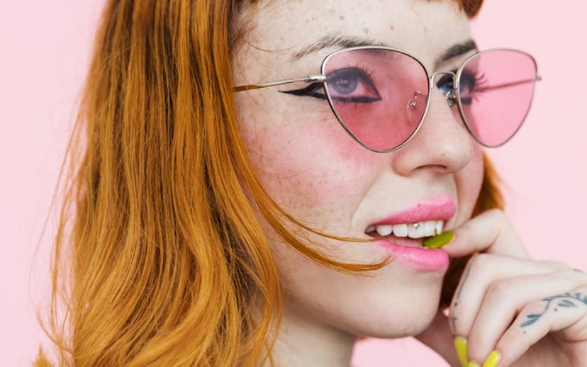 Alanna Pearl wearing pink sunglasses holding her hand to her chin and looking to the side