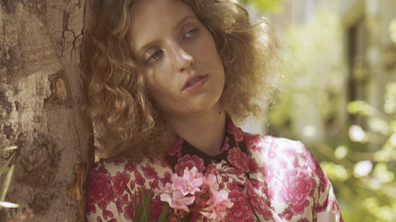 Petra Collins in a floral silk blouse, leaning against a tree