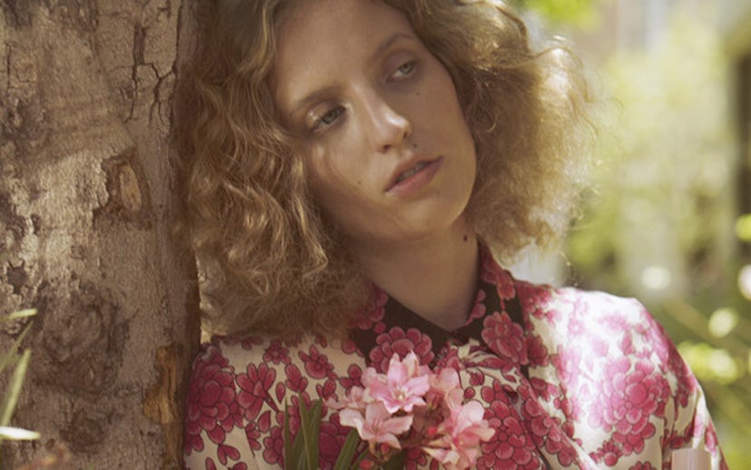 Petra Collins in a floral silk blouse, leaning against a tree