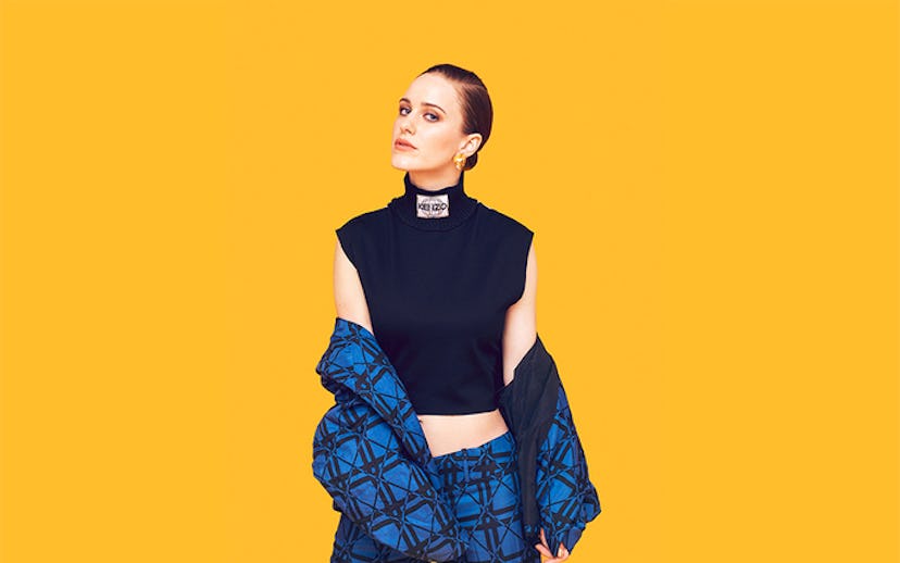 Rachel Brosnahan posing in a black sleeveless turtleneck and matching blue pants and jacket