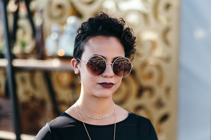 A girl with short black hair, a dark lipstick, and round sunglasses